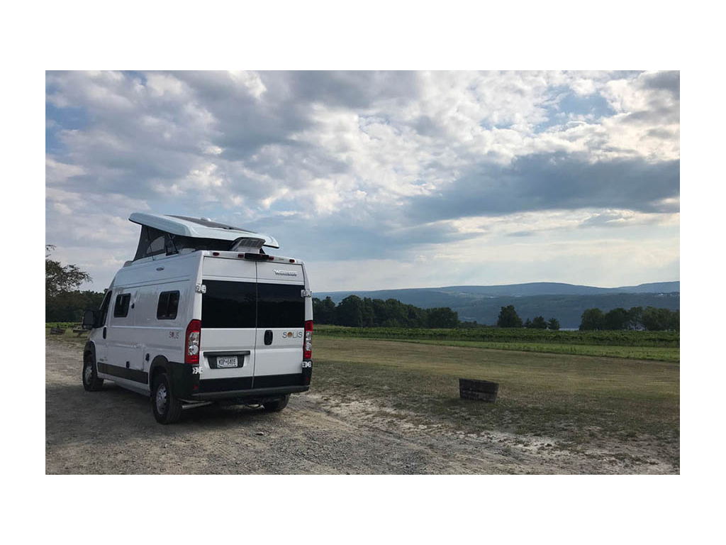 Winnebago Solis parked on gravel road with mountains and trees in distance