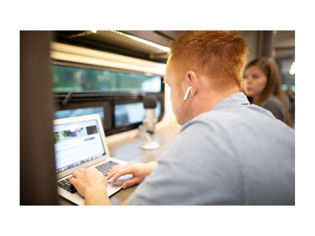 Alyssa and Heath working at work station in RV. Heath is wearing wireless headphones