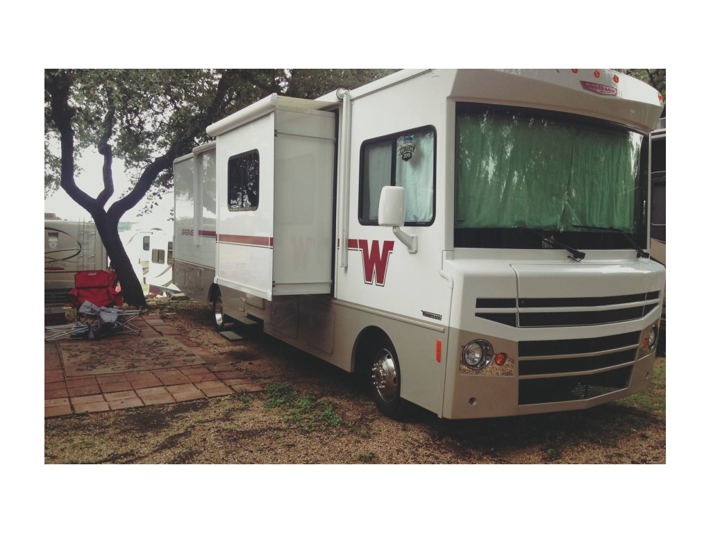 Winnebago Brave parked at campsite among other RVs and trees.