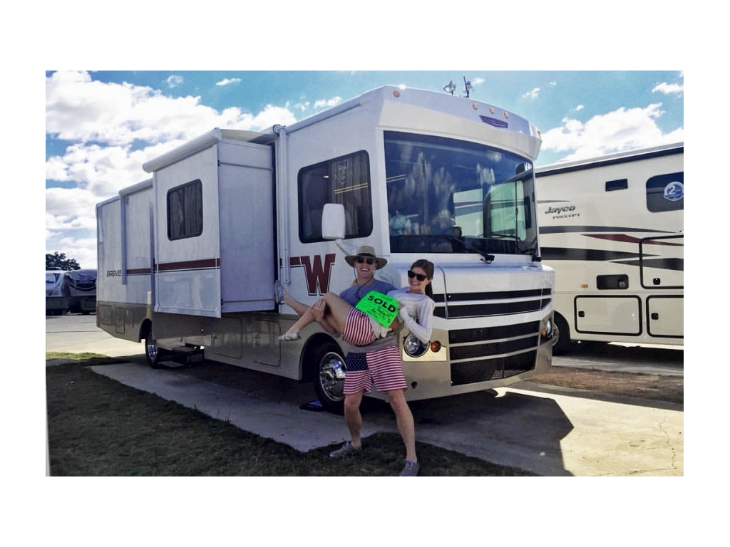 Heath and Alyssa holding a sold sign and smiling in front of their Winnebago Brave.