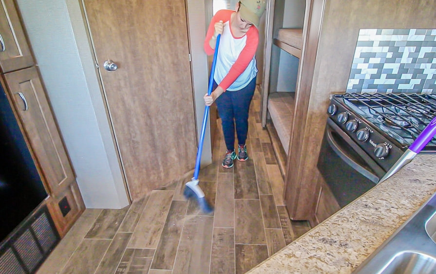 Young woman sweeps floor of Winnebago Intent for spring cleaning