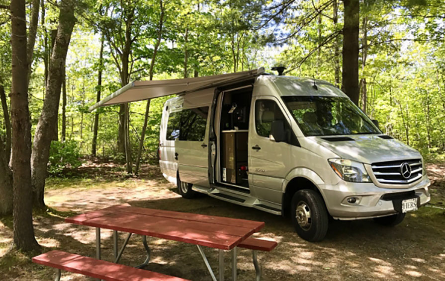Era parked in campsite under trees with awning extended