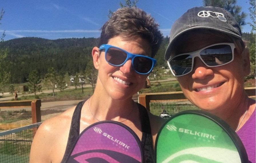 Ann and Lin holding up paddles and smiling for a selfie on pickleball court