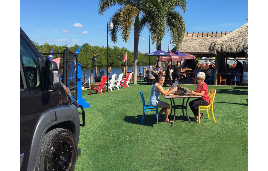 Chris and Noel sitting outside at a restaurant reading the menu. The Travato is near them.