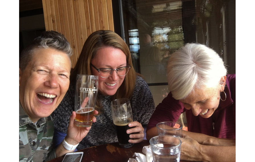 Noel, Jenny Van Atta and Chris all laughing while enjoying drinks at a table.