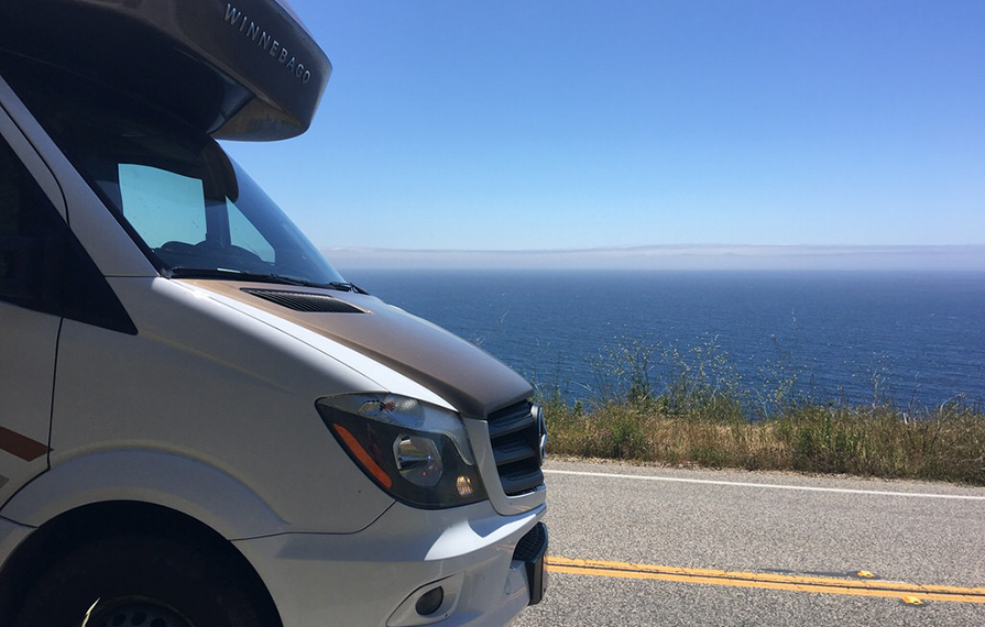 Front end of Winnebago View driving down road with view of ocean