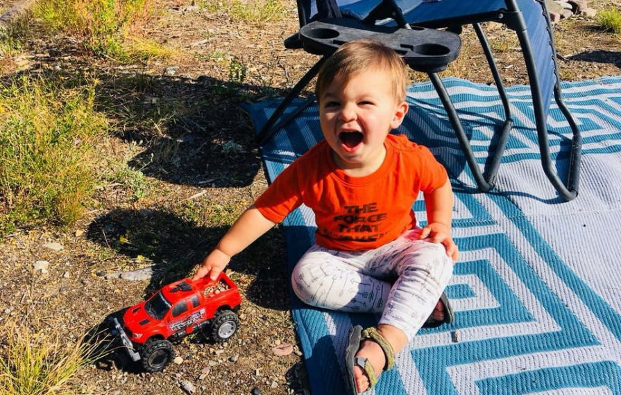 Caspian sitting on the ground outside playing with a toy truck