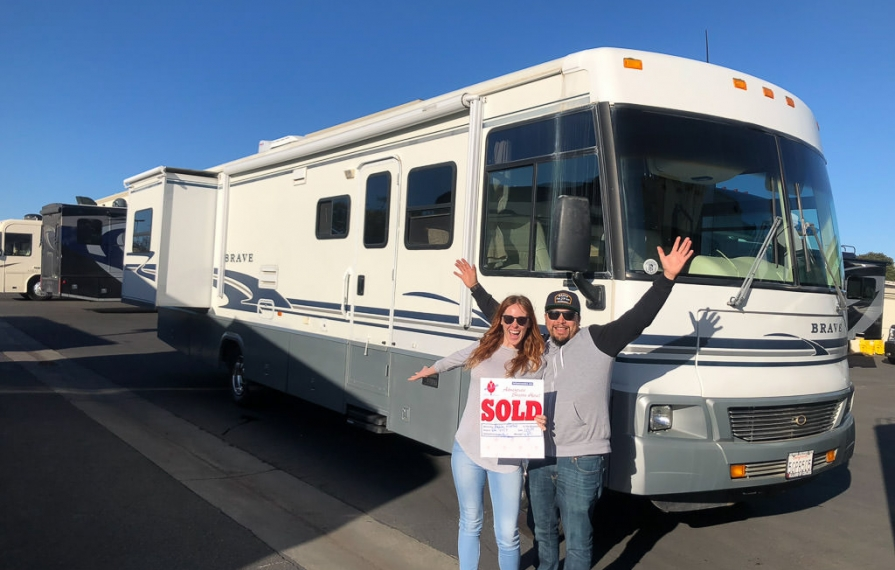 Ashley and Jessie holding sold sign standing in front of Winnebago Brave