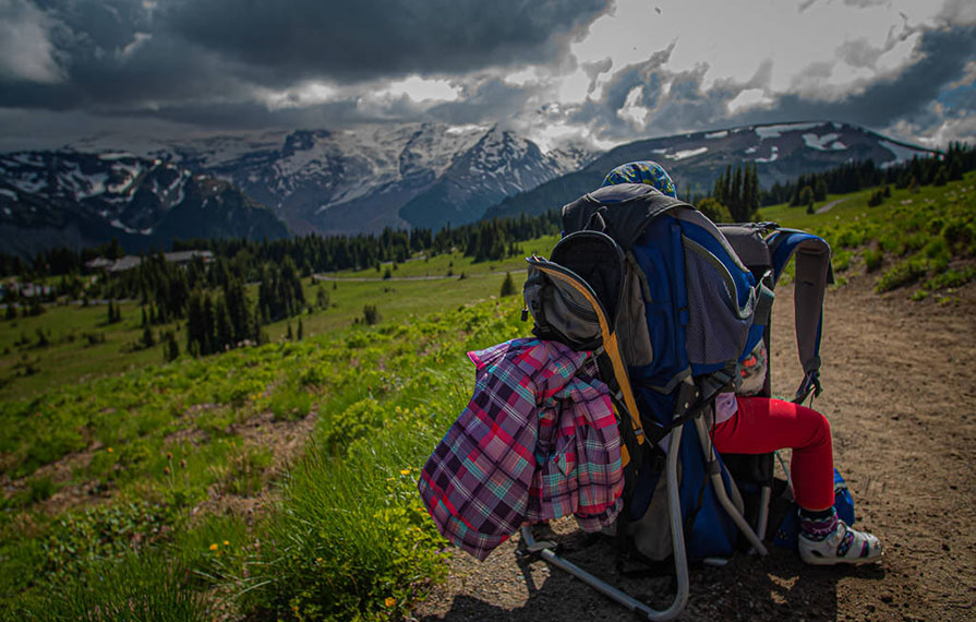 Hiking backpack on the ground with one of the kids and mountains in the background