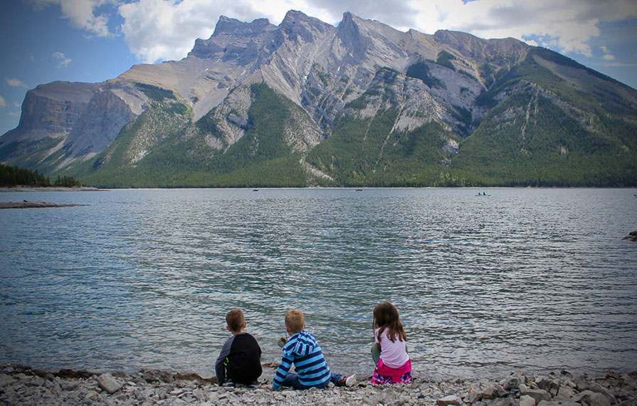 Three kids sitting next to Lake Minnewanka