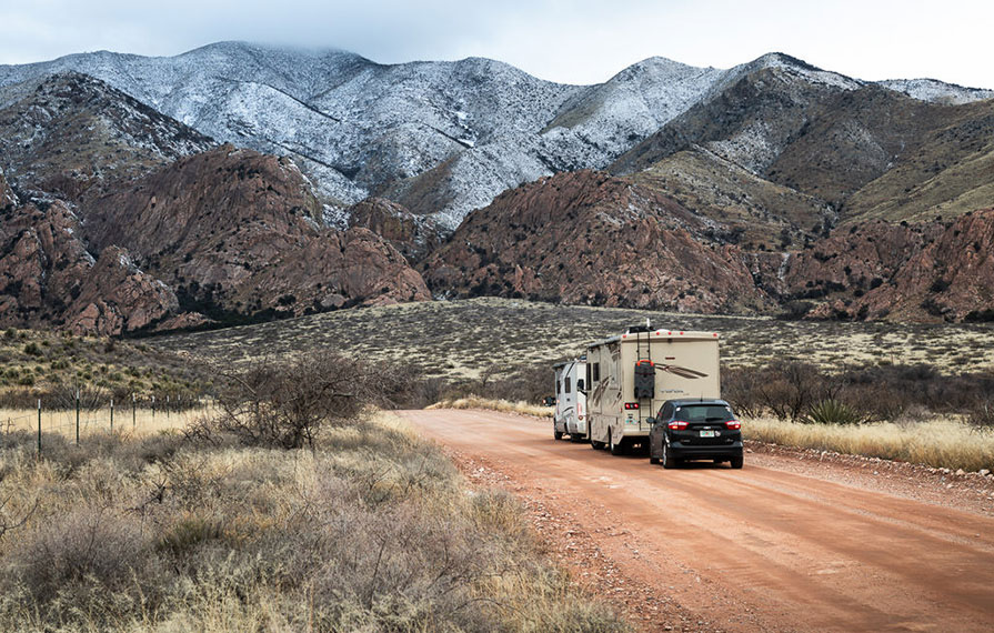 Trend, Vista and tow car driving down dirt road with snow capped mountains in front of them