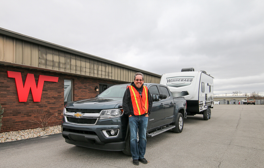 Traveling Robert standing in front of Winnebago Towables plant with truck pulling trailer