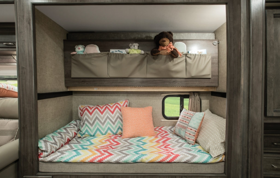 Bunk space with colorful bedding and kids stuffed animals tucked in compartment above.