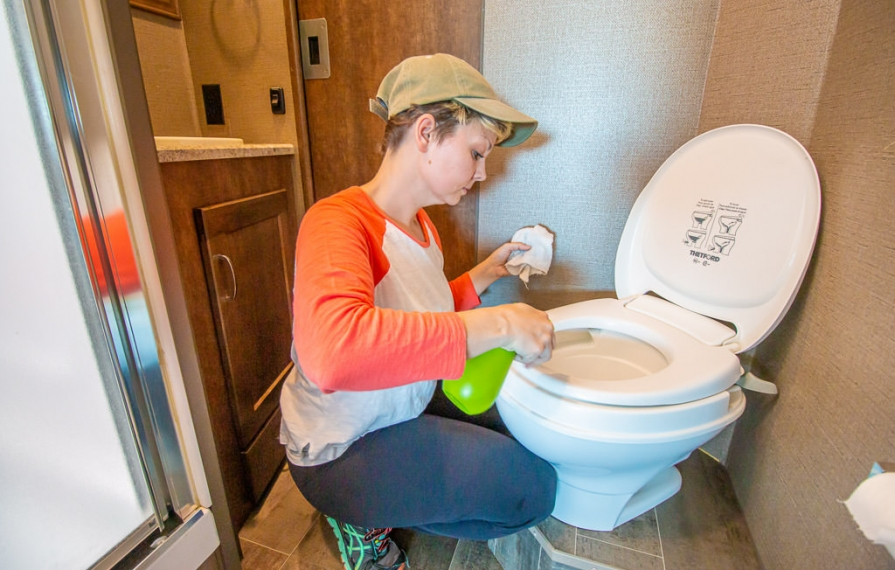 Young woman scrubs down the RV toilet for spring cleaning