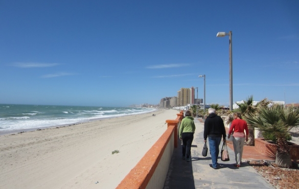 People walking along Playa Bonita Beach towards row of resorts.