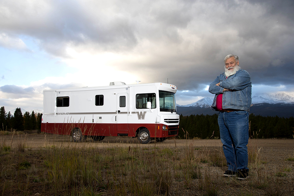 Man standing in front of Winnebago brave with mountains in the background.
