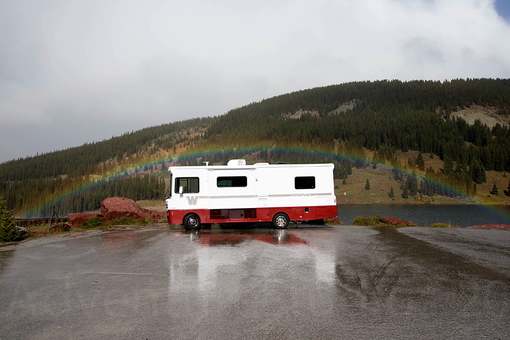 Winnebago Brave parked on pavement with rainbow over the top of it. 