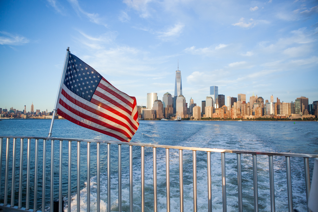 Manhattan skyline from back of a boat with American flag flying.
