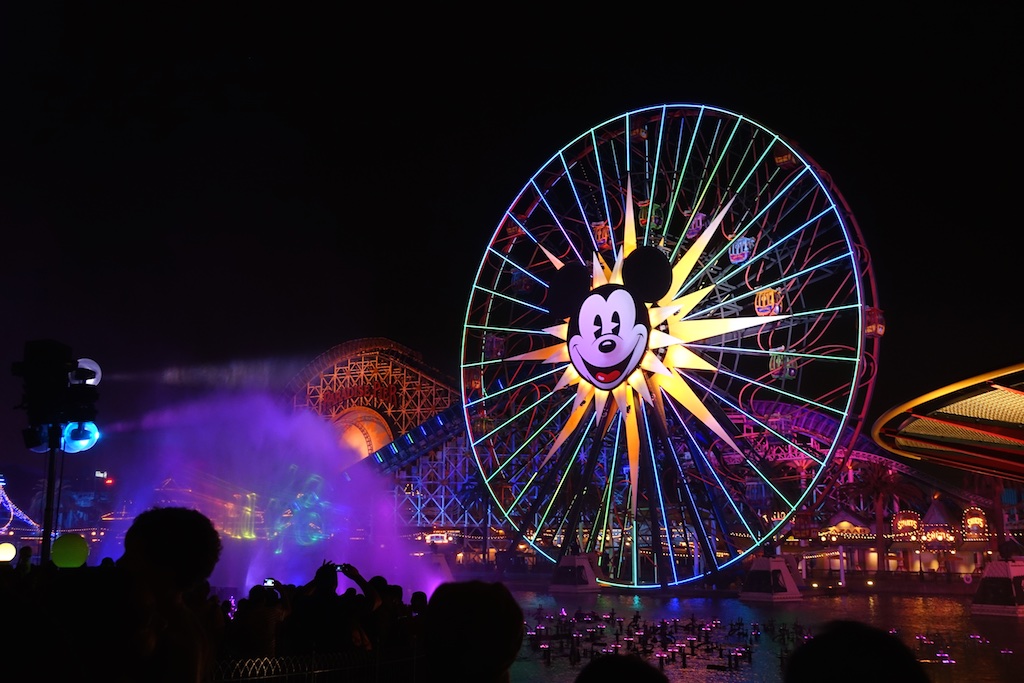 The face of Mickey Mouse lit bright on the ferris wheel against the night sky.