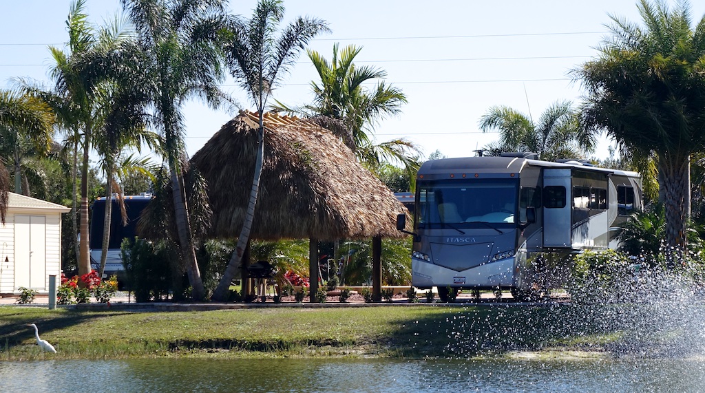 Winnebago Ellipse parked in RV site with tiki hut next to it and palm trees surrounding.