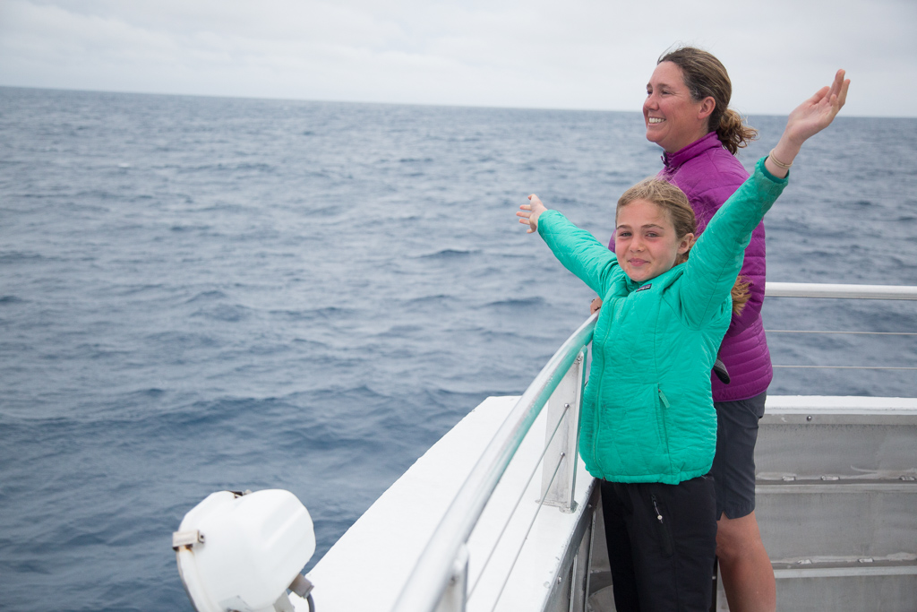 Kathy standing next to Abby, who has her arms stretched wide, at the back of a boat.