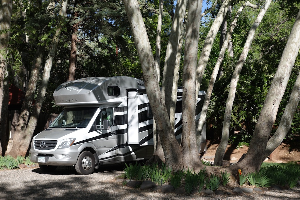Winnebago Itasca Navion parked in shaded campsite.