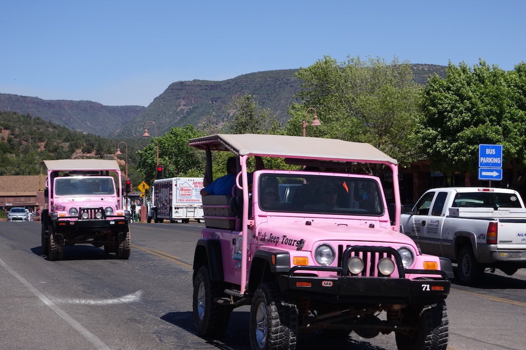 Pink Jeep Tour vechicles driving down the road with canyons in the background.