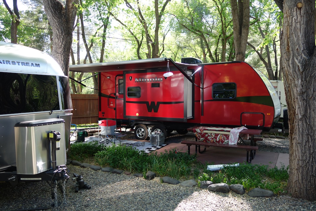 Red Winnebago Minnie Winnie parked in tree shaded campsite.