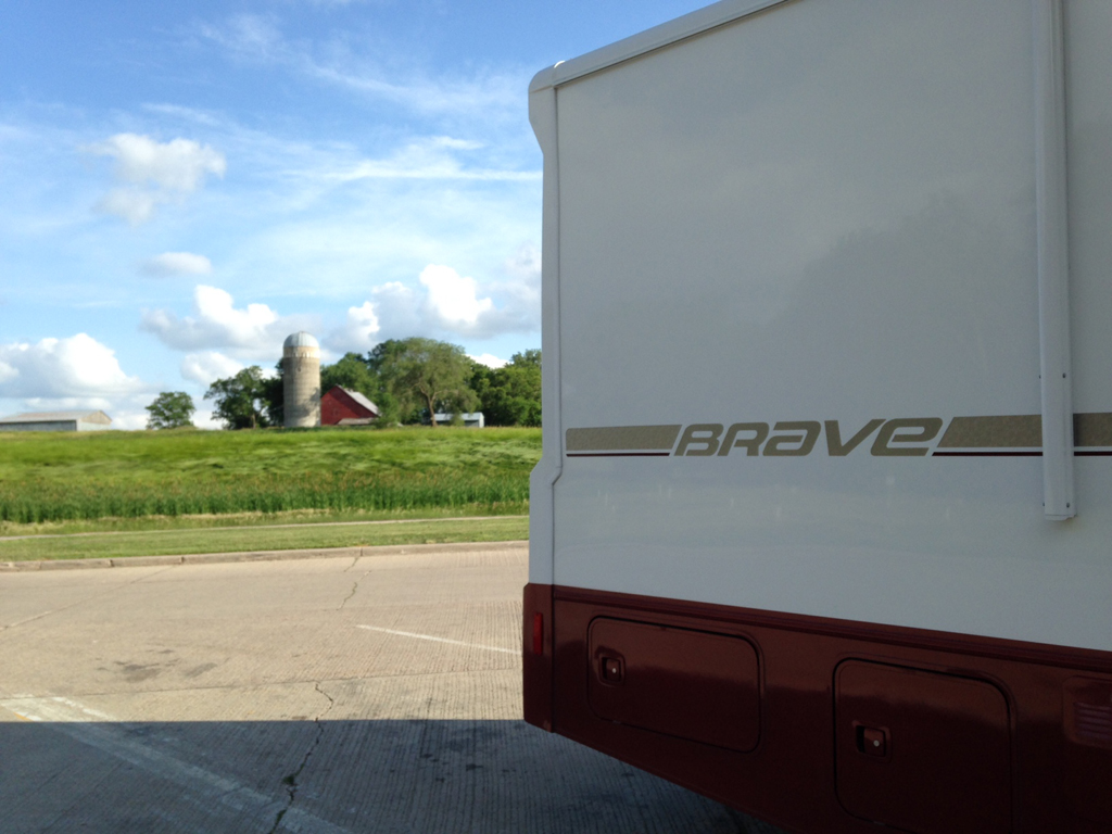 Winnebago Brave in parking lot with farm in the background.