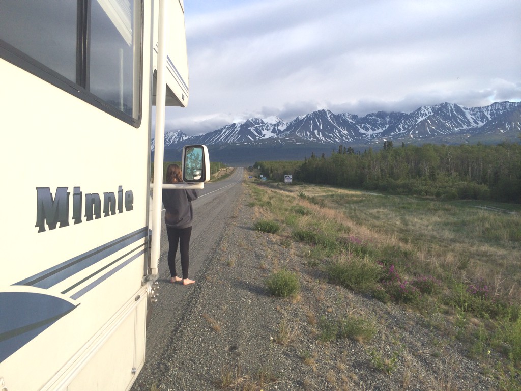 Woman standing in front of a parked Winnebago Winnie Minnie taking a photo of the mountains ahead.