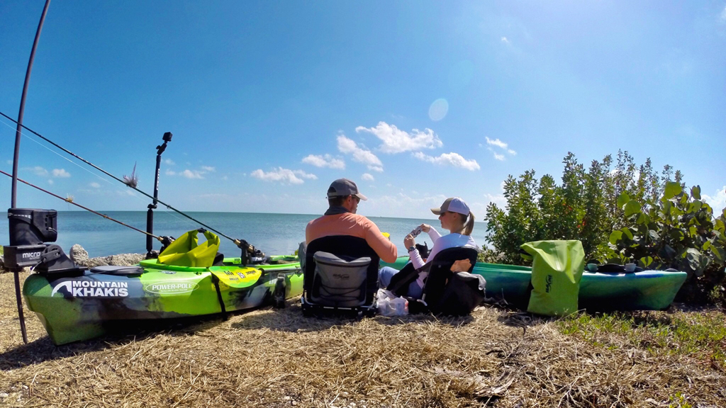 Damon and Ashley resting on the shore eating lunch with kayak and gear around them.