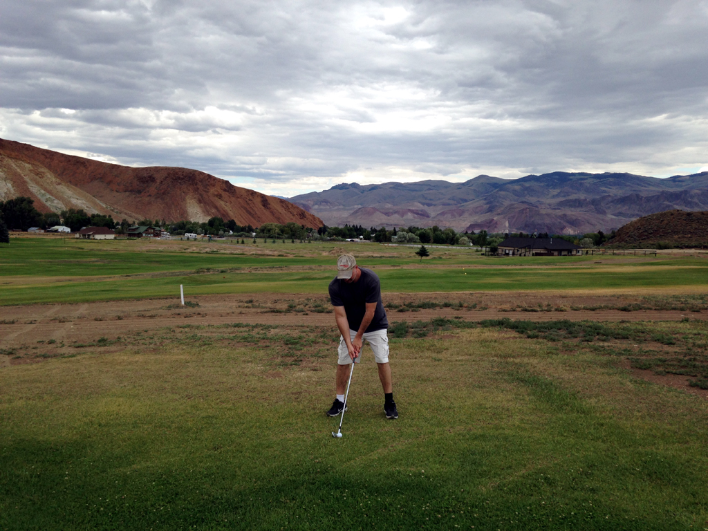 Man ready to tee off at the golf course with cliffs and mountains in the background.