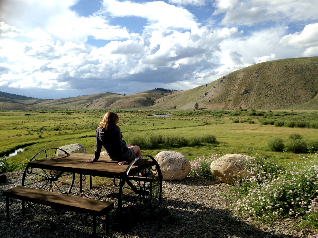 Woman sitting on a picnic table looking out across the plains and hillside.