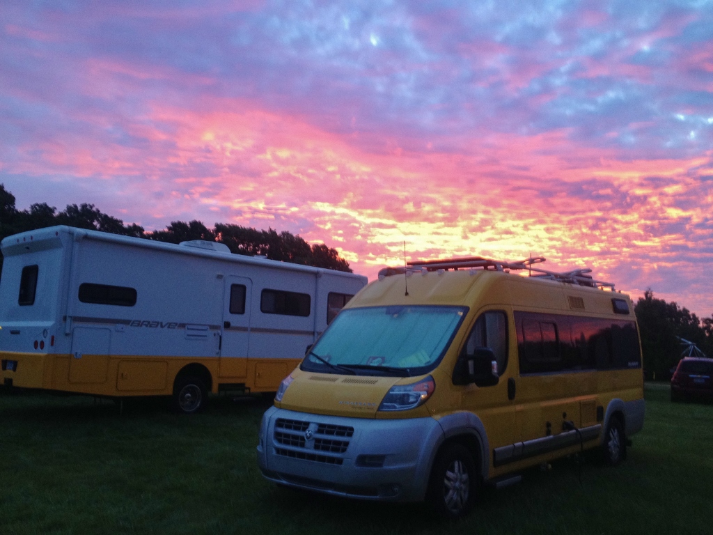 Yellow Winnebago Travato parked next to Winnebago Brave with yellow detailing with beautiful sunrise overhead.