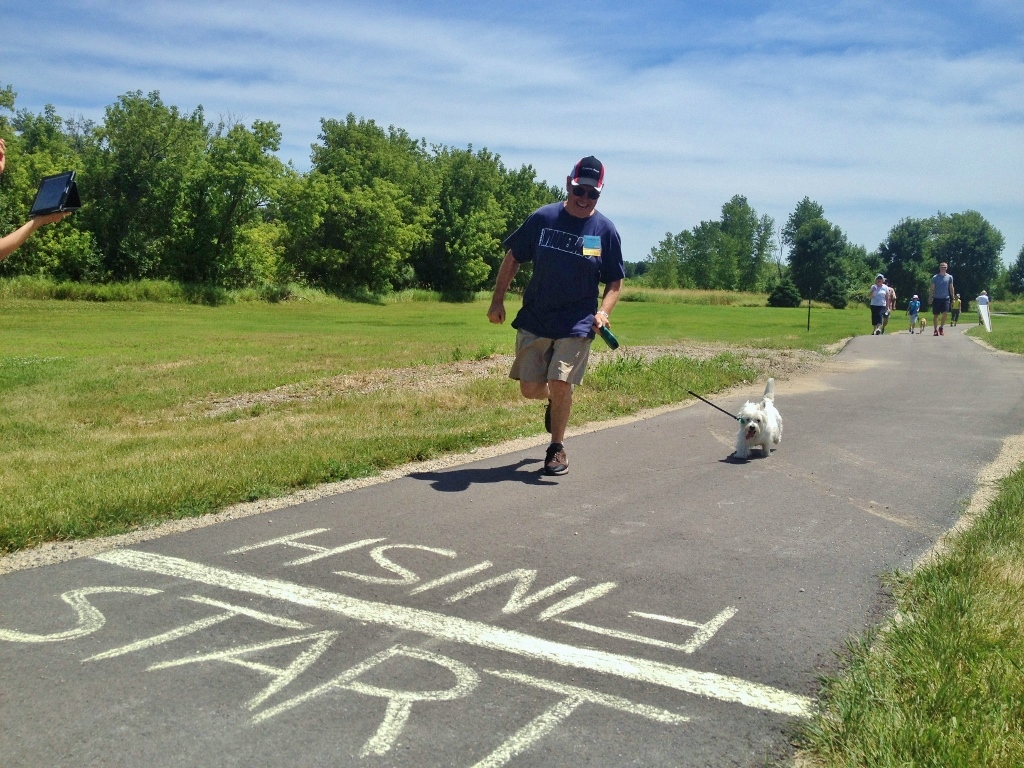 Man and dog heading toward finish line on a path.