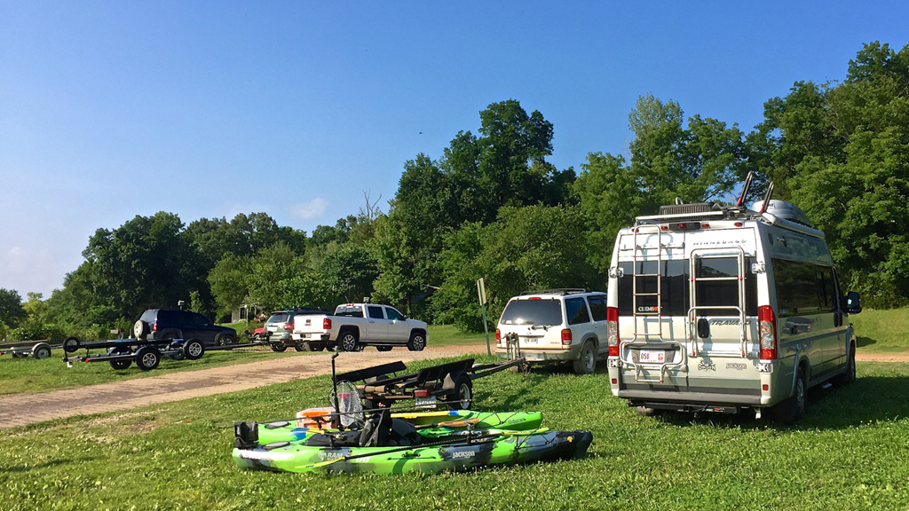Travato parked in grass with kayaks and gear behind it