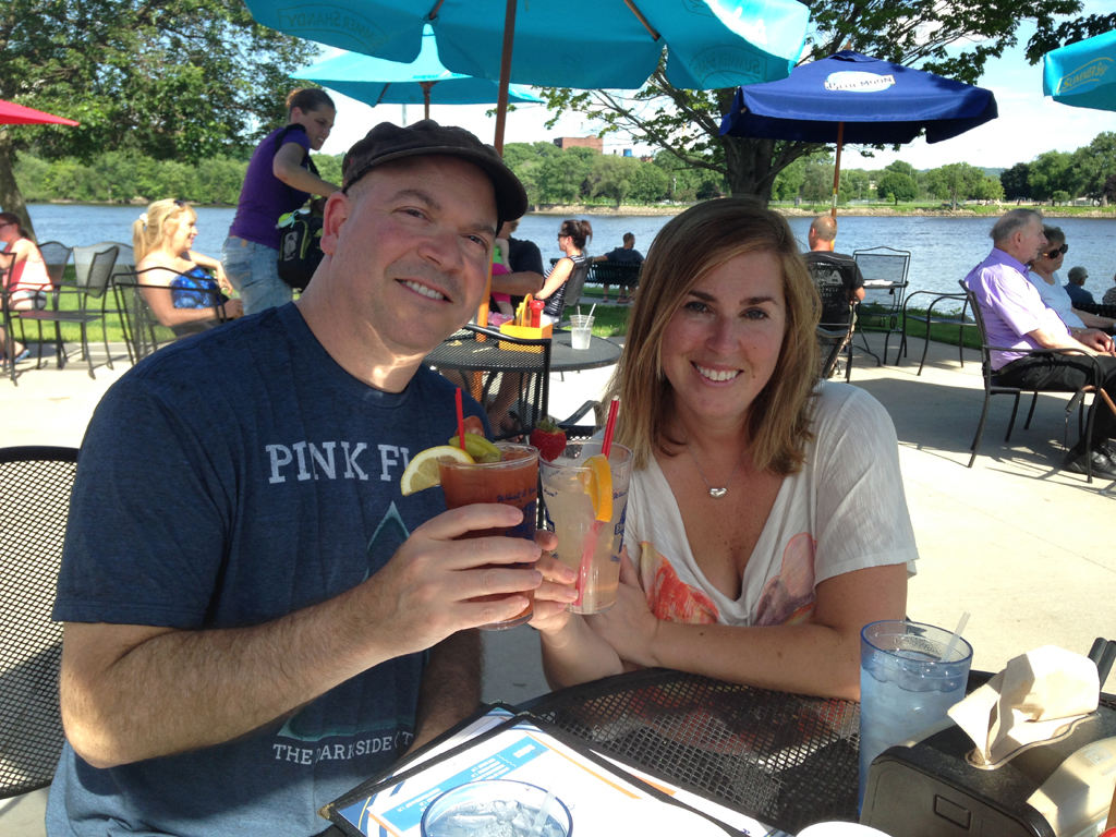 Couple smiling with drinks on a patio next to water.