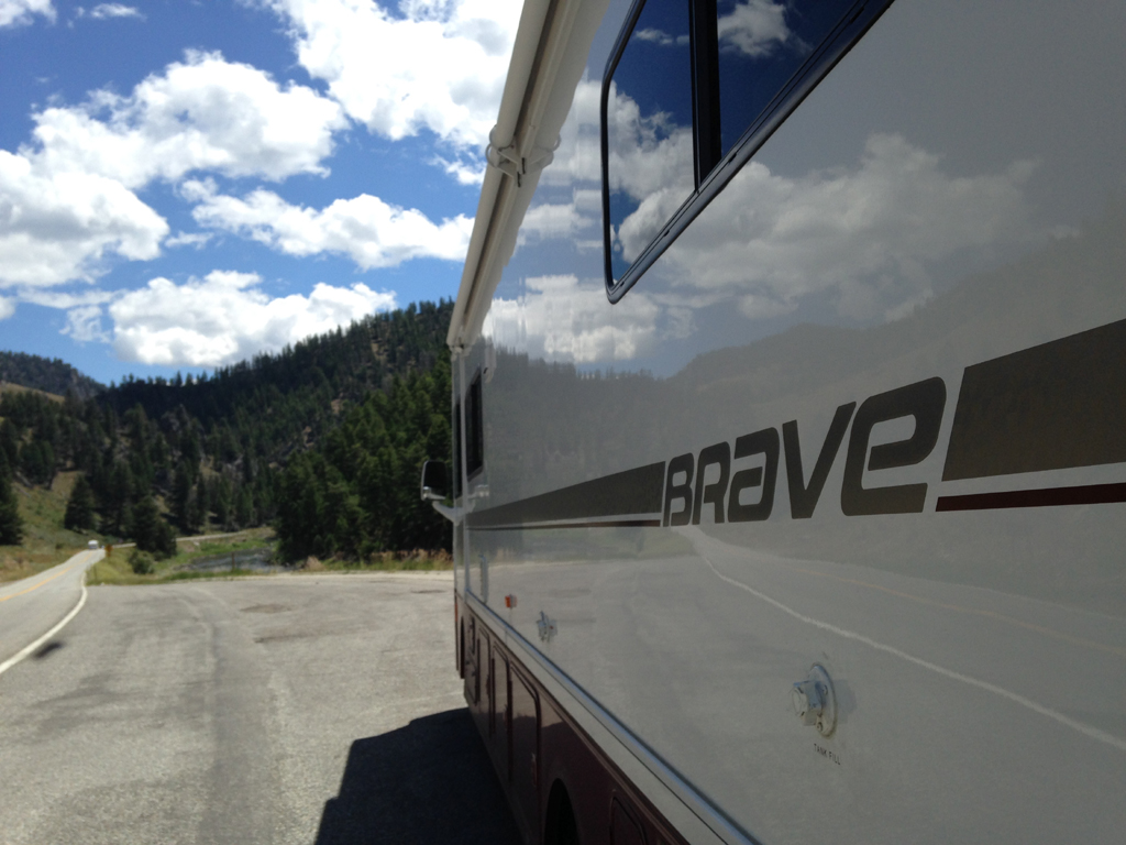 Winnebago Brave parked alongside the road with tree covered hills ahead.