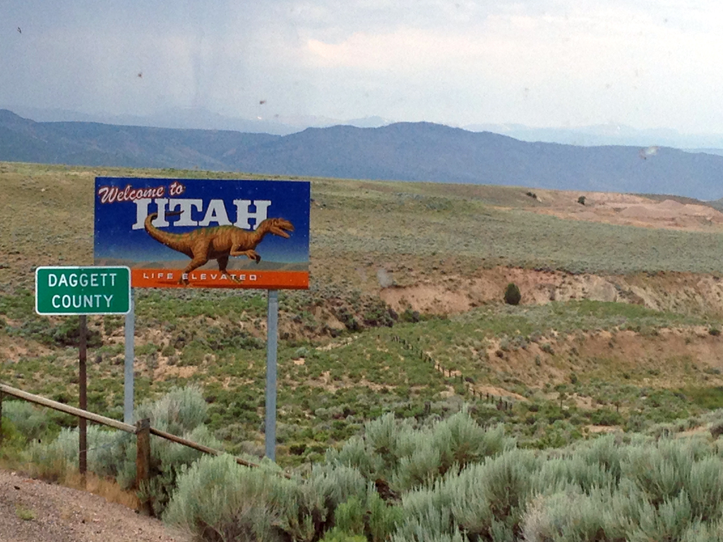 "Welcome to Utah" sign with rough terrain in background.