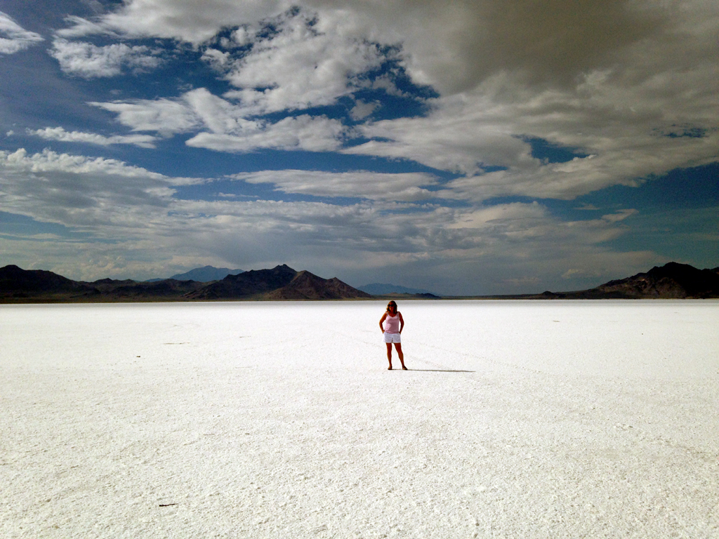 Woman standing on white sands with mountains in background.