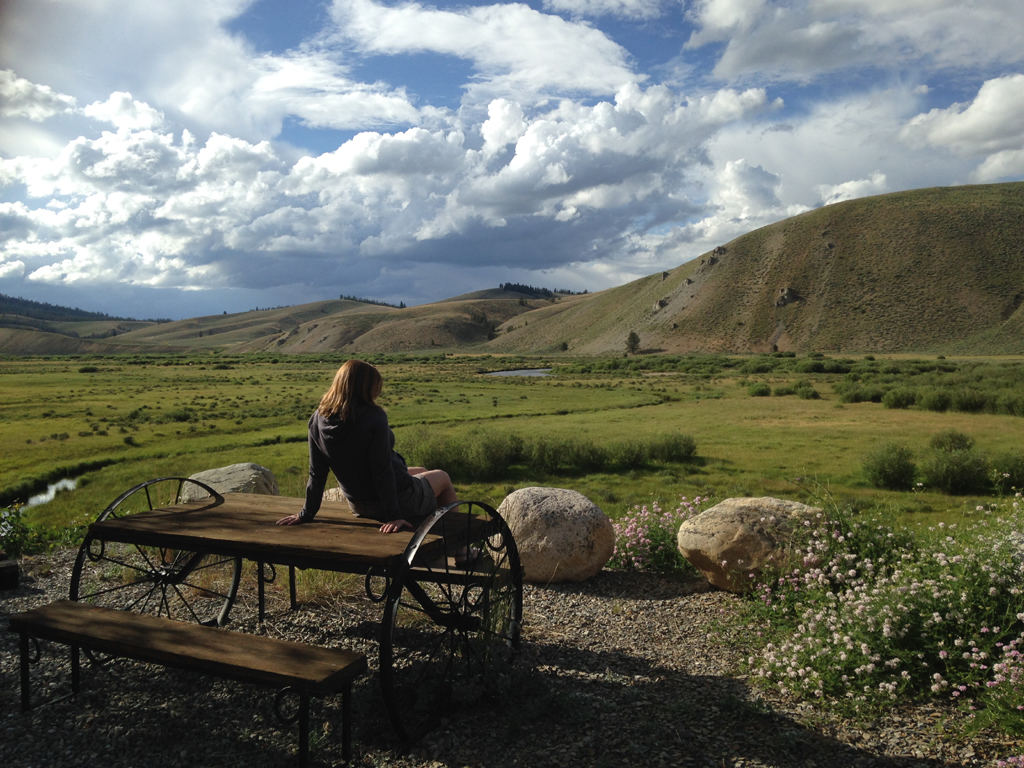 Woman sitting on picnic table looking out over grassy hillsides.