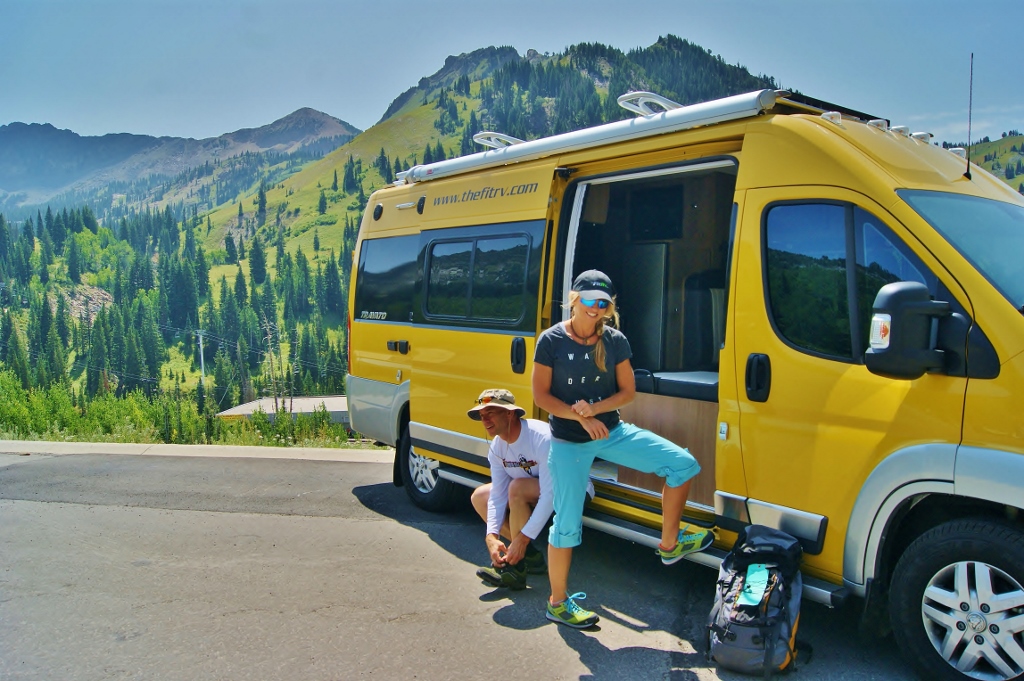 James and Stef at the side of their Winnebago Travato with mountains in the background.
