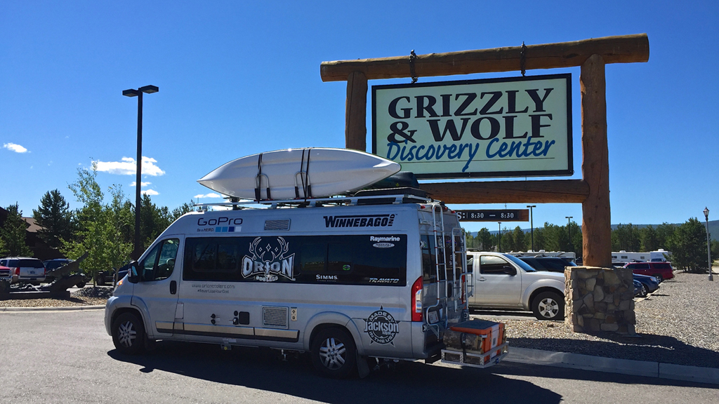 Winnebago Travato parked in front of Grizzly & Wolf Discovery Center sign.