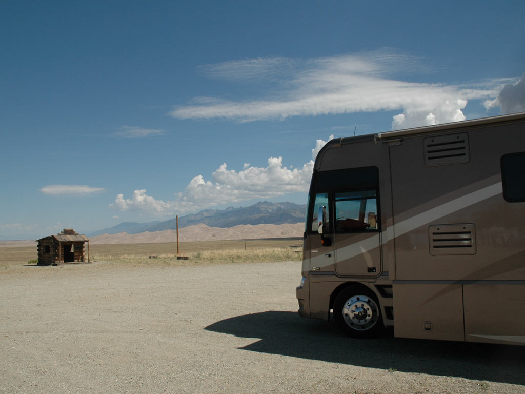 Motorhome parked in empty lot with sand dunes in view.
