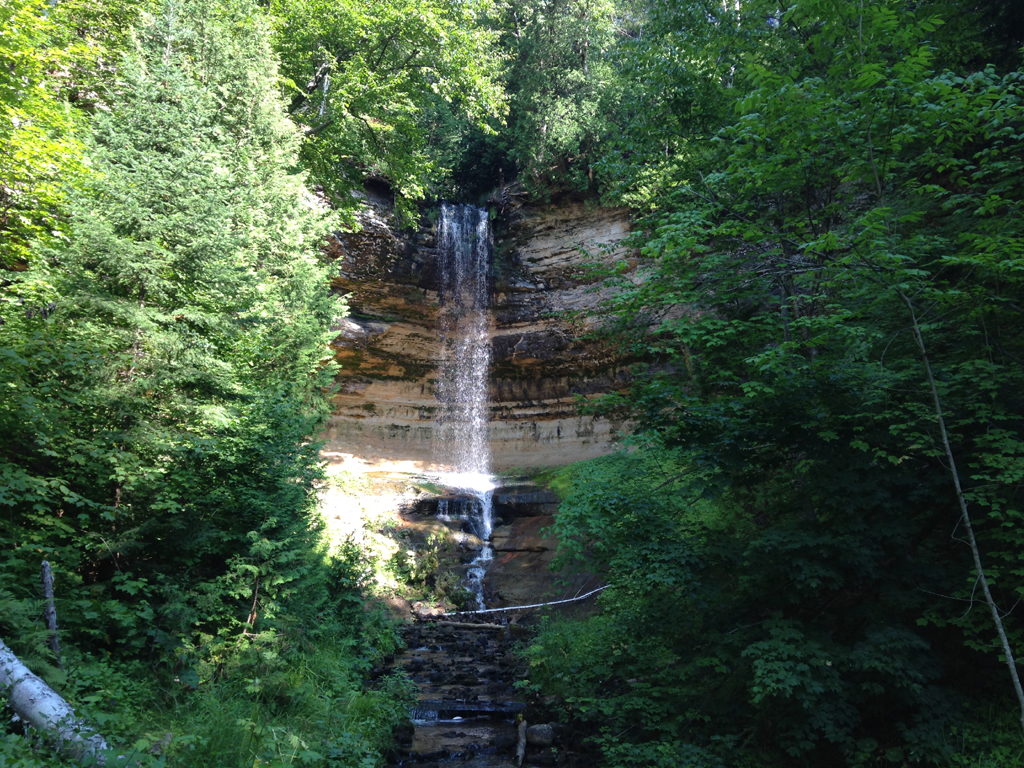 Munising Falls spilling over the side of a rocky cliff with lush green trees on either side.