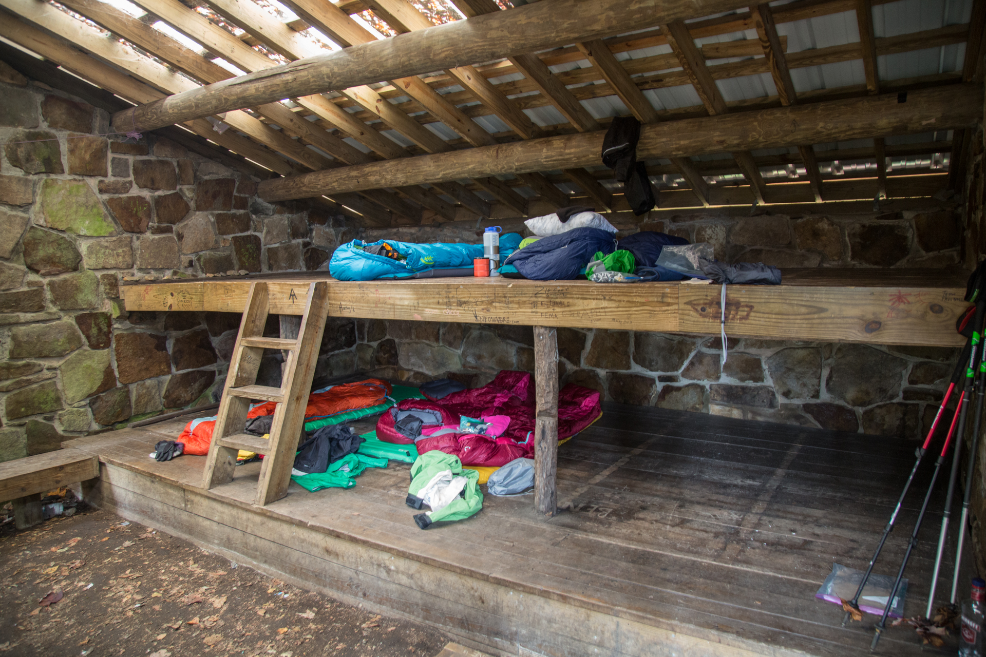 Interior of the shelter with makeshift bunks of wood and gear spread across.