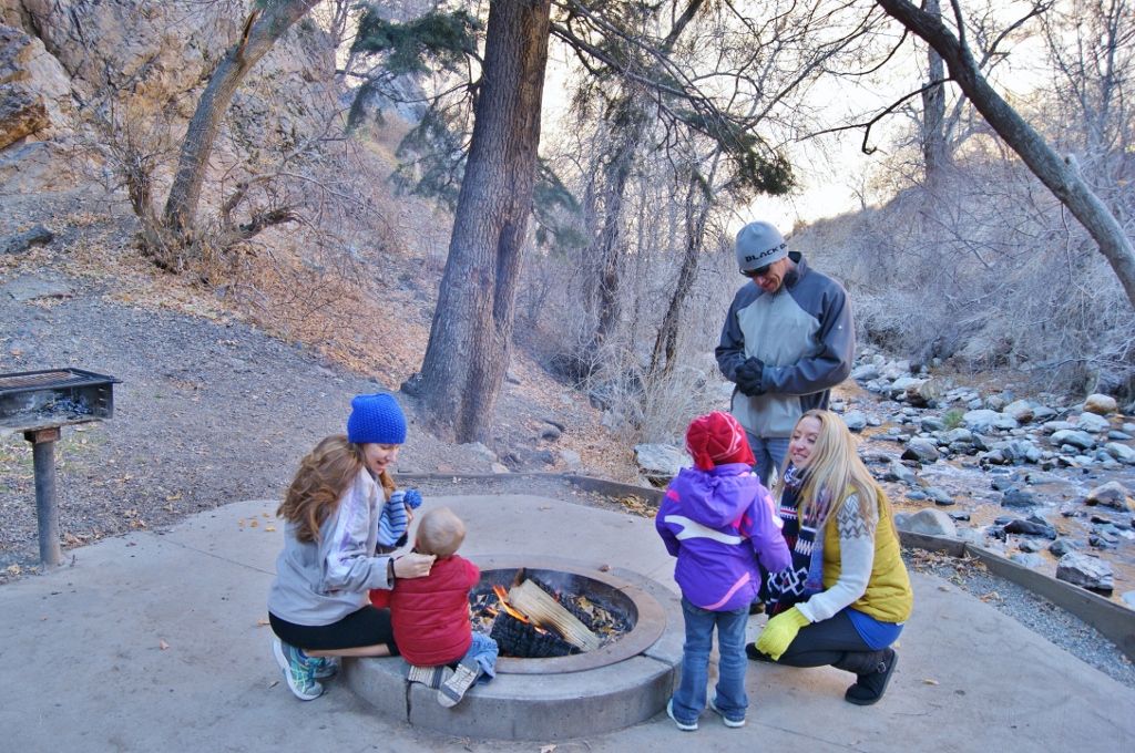 James, Stef and family members huddled around a campfire with stream flowing past in the background.