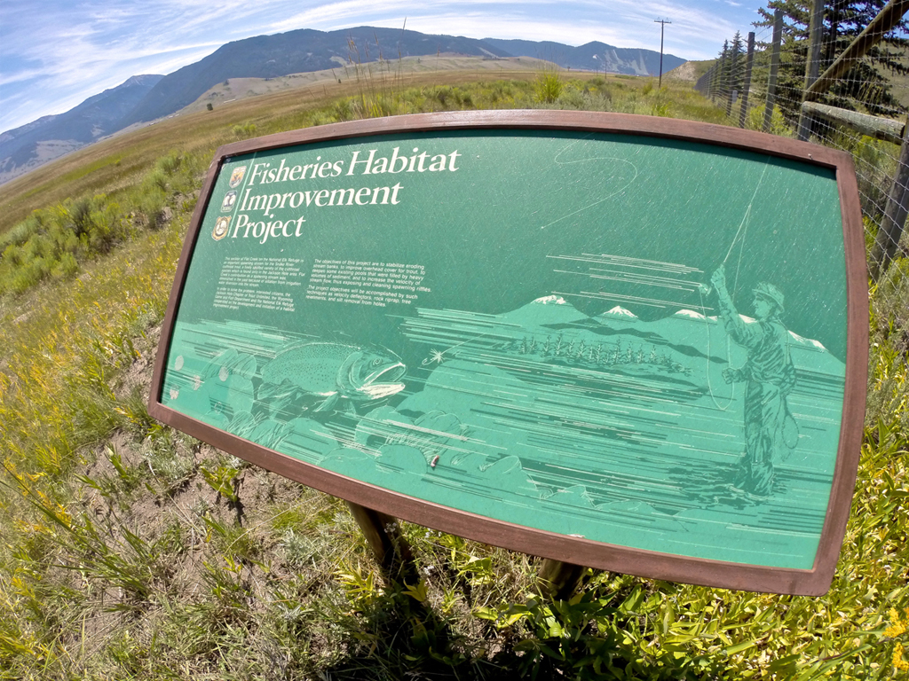 Sign in field that reads "Fisheries Habitat Improvement Project" with mountains in the distance.