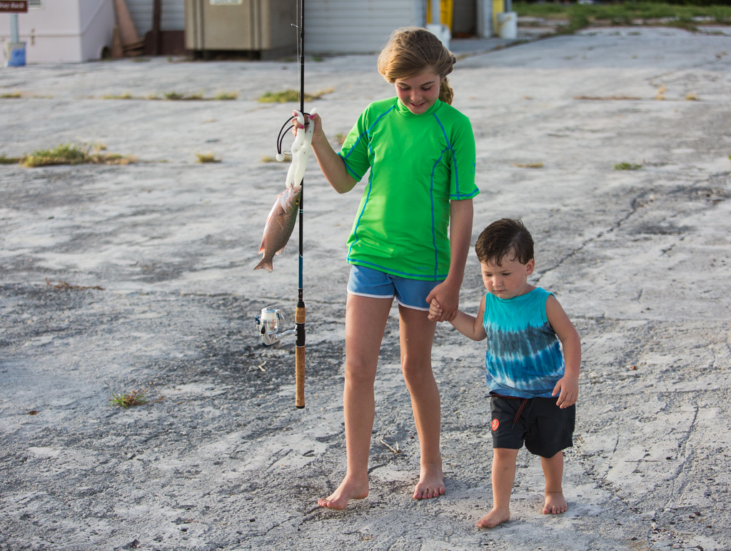 Abby holding a fishing pole with fish still attached in one hand and holding little Tucker's hand in the other.