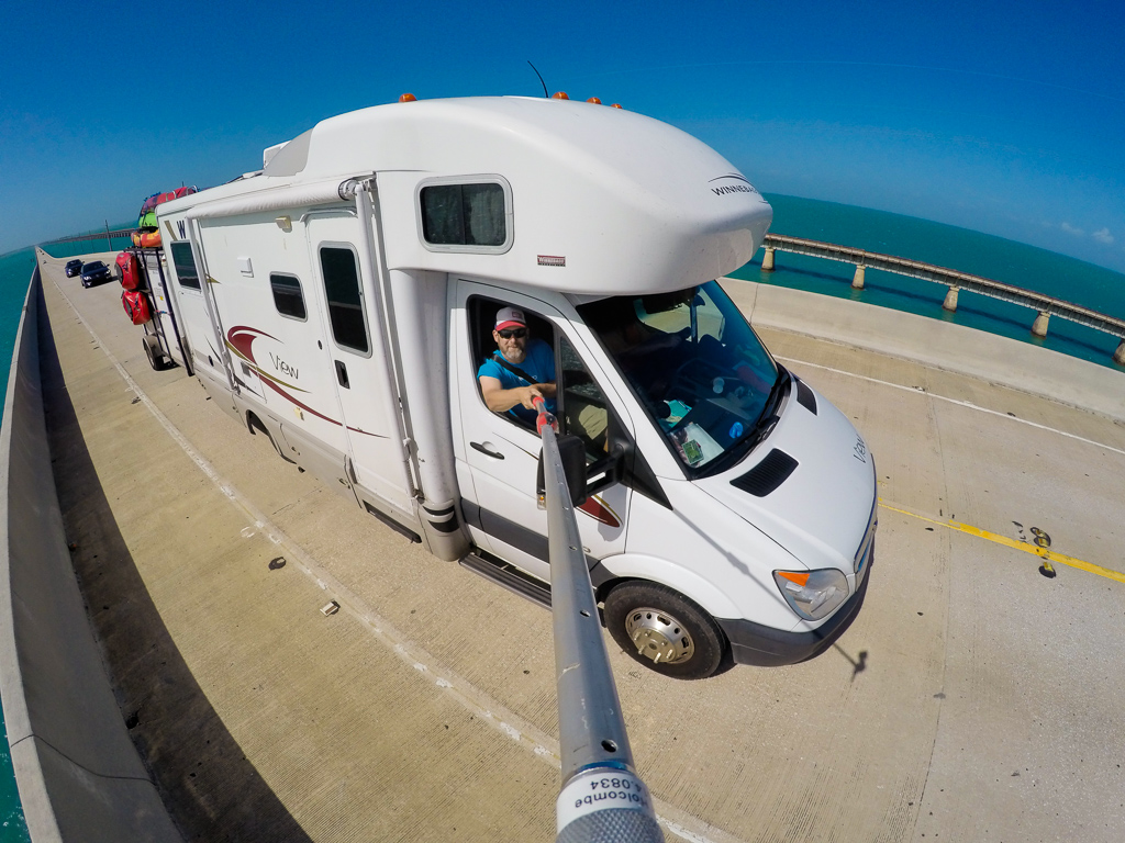 Peter taking a selfie of their Winnebago View with toy hauler attached going across a bridge over the water..